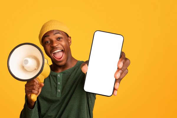 Cheerful Black Guy Shouting In Loudspeaker And Pointing At Camera Cheerful Black Guy Shouting In Loudspeaker And Pointing At Camera, Excited African American Man Holding Megaphone, Making Announcement, Standing Isolated Over Yellow Background, Copy Space